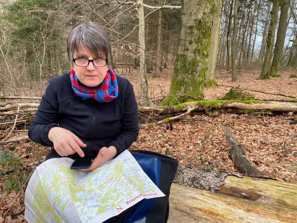 Frau sitzt auf Baumstämmen und schaut auf ihr Handy und eine Karte