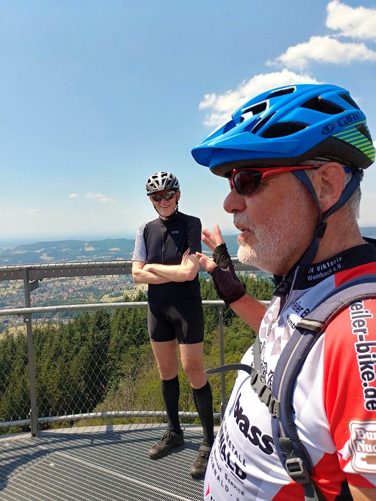 Zwei Mountainbiker auf einer Aussichtsplattform mit Panorama im Hintergrund