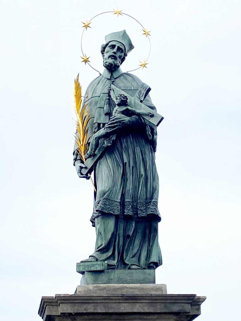 Statue des Heiligen Nepomuk auf der Karlsbrücke in Prag - mit goldenem Kranz, fünf Sternen und goldener Märtyrerpalme in der Hand.
